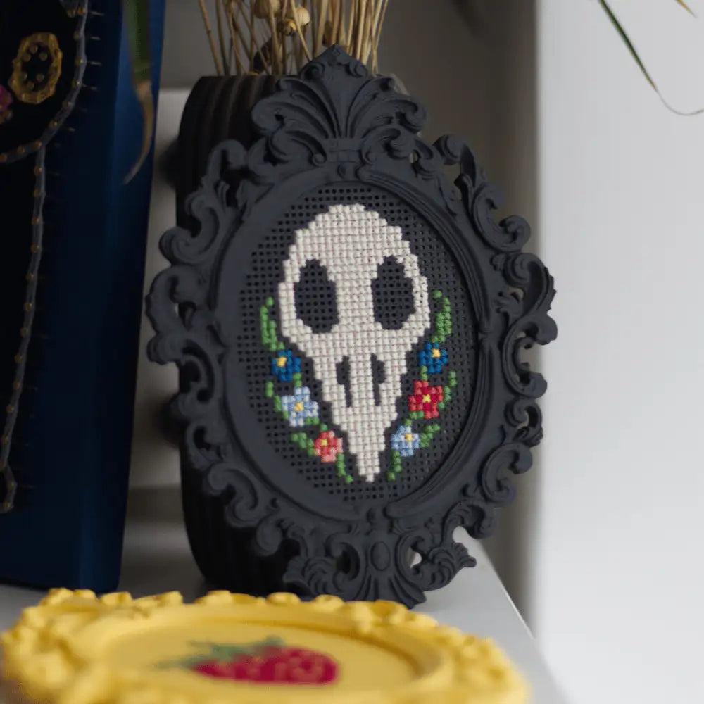 Black baroque cross stitch frame with a stitched skull and floral design