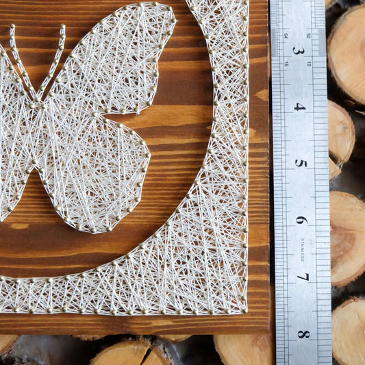 Close-up view of butterfly string art pattern design on wood with a ruler for scale, showcasing the intricate string work and circular border detailing.
