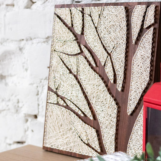Side view of the completed tree silhouette string art, highlighting the texture and depth of the ivory thread on the wooden board, as part of a craft kit for adults.