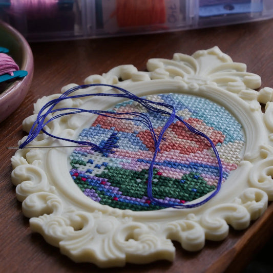 Baroque oval cross stitch frame with stitched landscape design and embroidery thread in progress