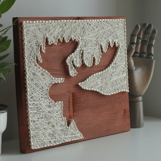 Finished moose silhouette string art made with ivory thread and nails on a stained wooden base, DIY string art kit for adults displayed on a shelf with decor.