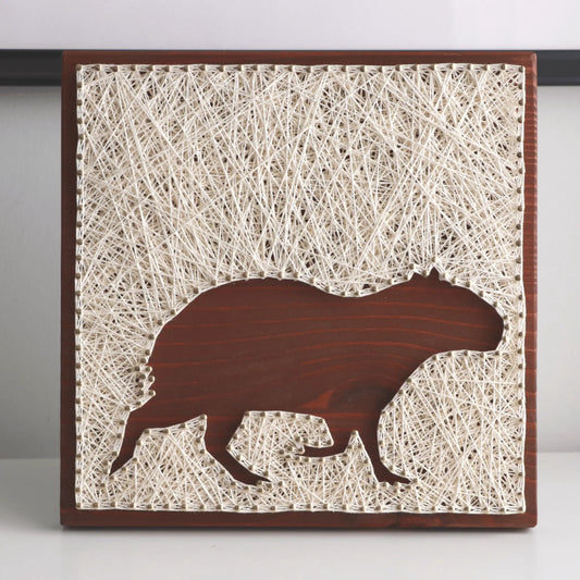 Artistic depiction of a capybara silhouette on string art with a wooden frame.