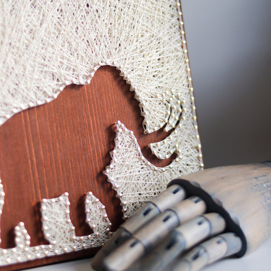 Woolly mammoth string art pattern with a wooden hand prop showcasing its handcrafted details. A charming addition to DIY projects.