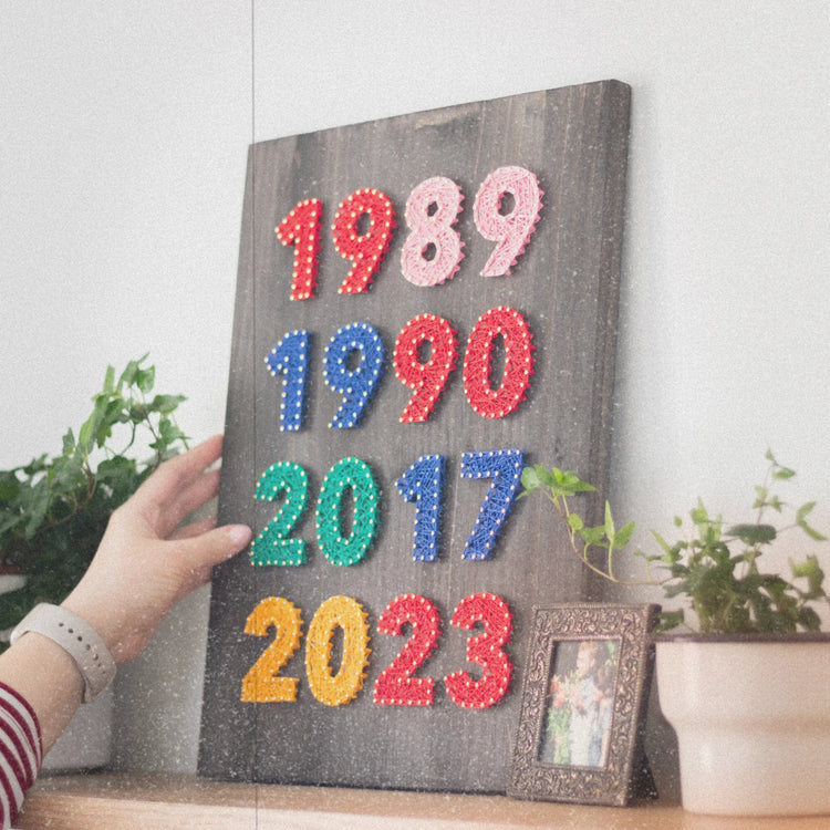 string art sign on dark wood base with red, pink, blue, green and yellow birth years