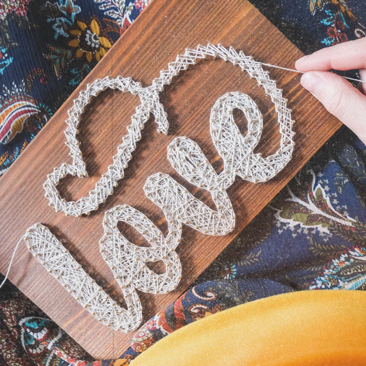 love text string art sign on brown wood base being made