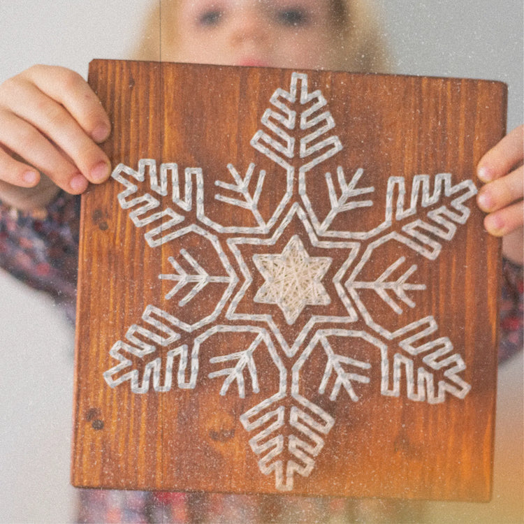 delicate string art snowflake on brown wood base held by a blond girl