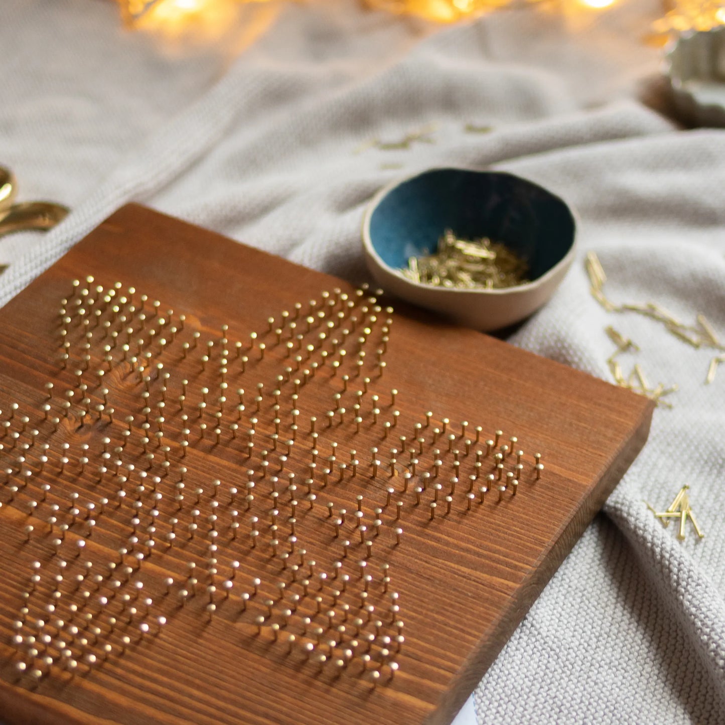 Crafting process of the snowflake string art sign, with brass nails and white thread in the beginning stages, made using GoodStrings' snowflake string art pattern.