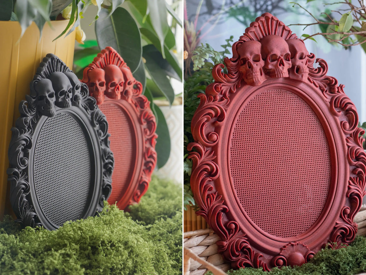 Black and red three skulls cross stitch frames printed in PLA, displayed among plants and moss
