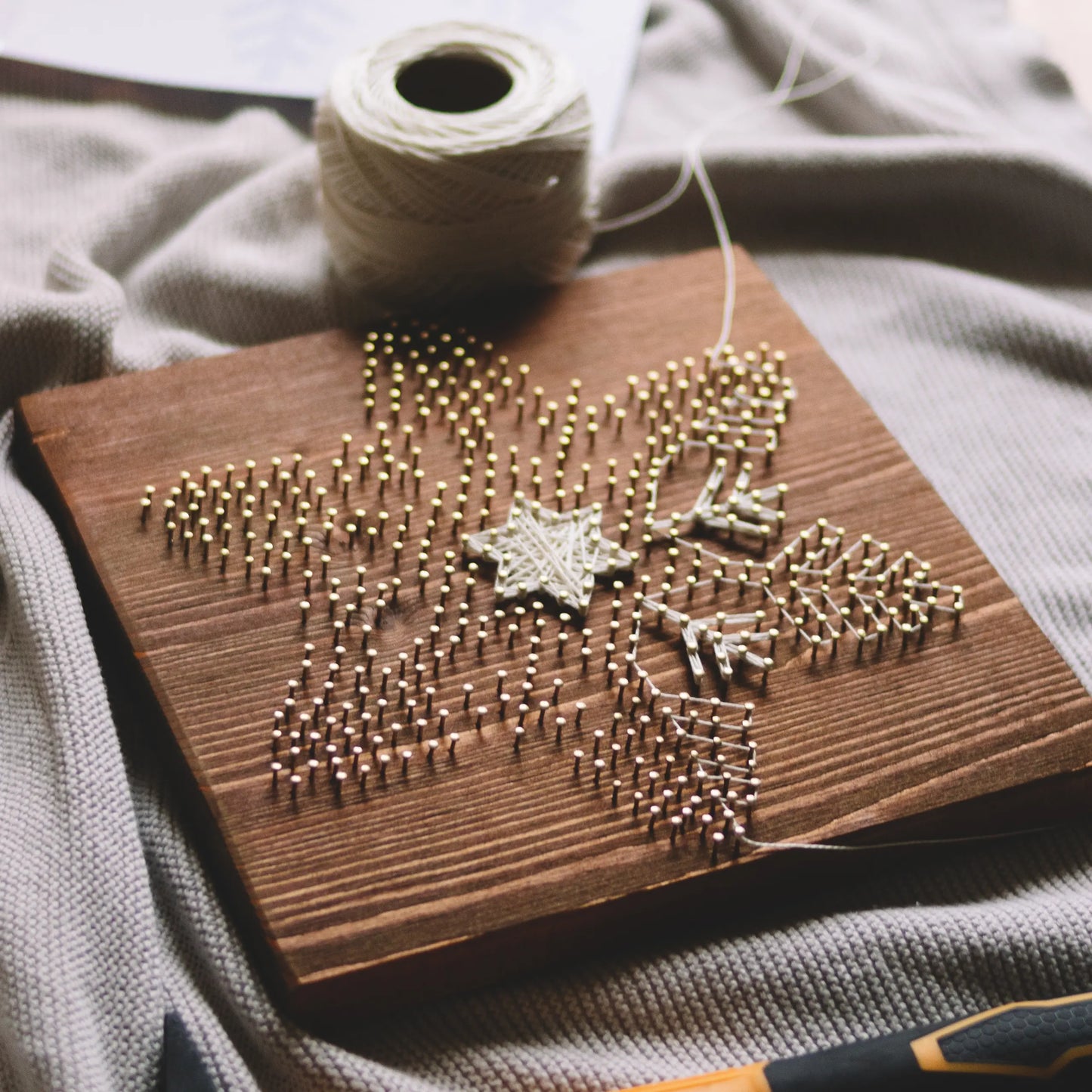 Crafting process of the snowflake string art sign, with brass nails and white thread in the beginning stages, made using GoodStrings' snowflake string art pattern.