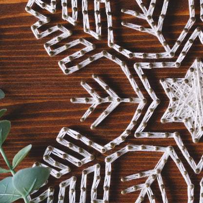 Close-up of the details in a snowflake string art piece, showcasing the intricate threading around the nails on a wooden board.