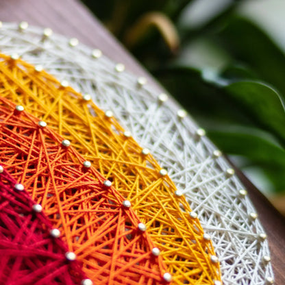 Close-up of a vibrant pumpkin string art pattern, showcasing a mix of white, yellow, orange, and red threads to create a colorful, layered look on a wooden base.