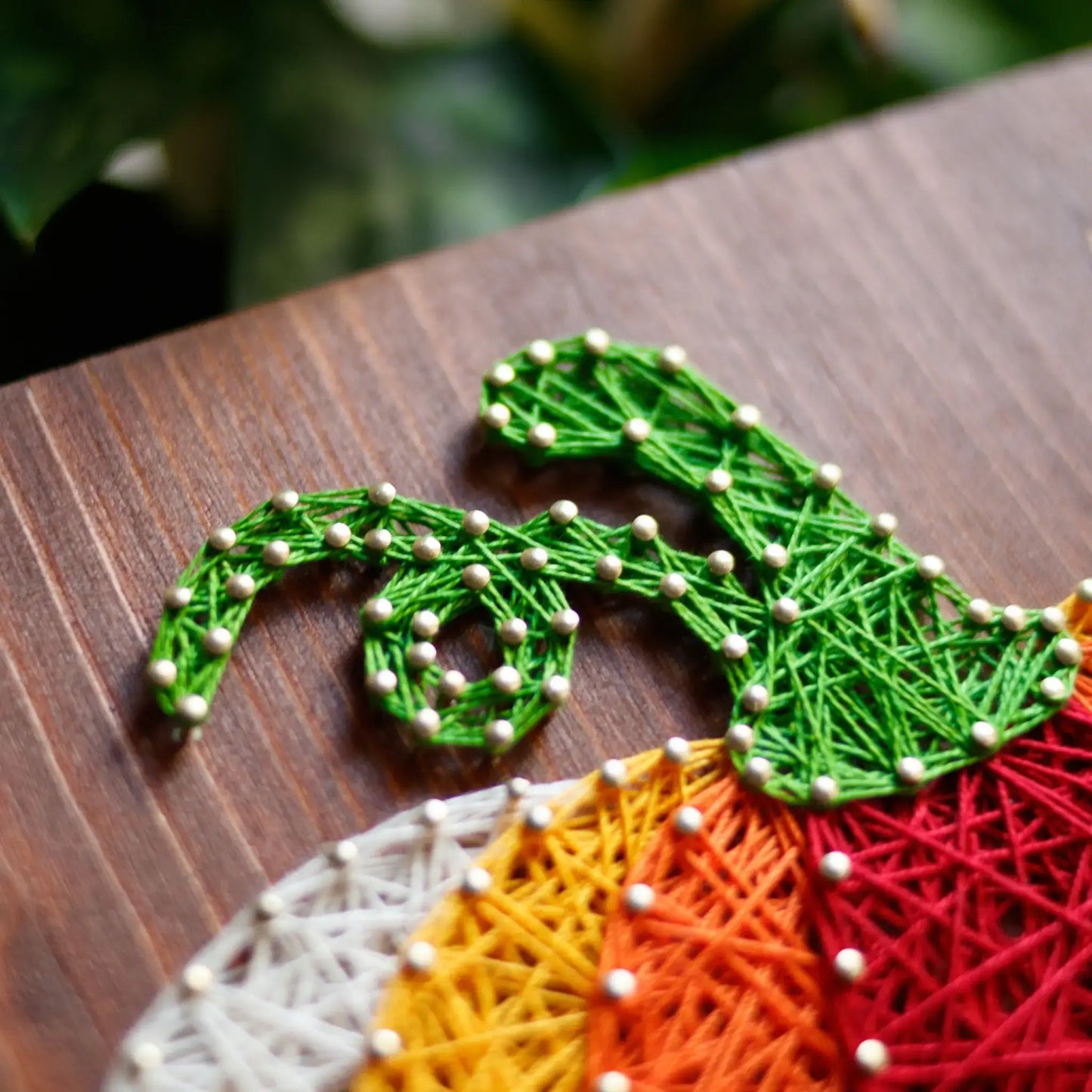 A detailed shot of the green vine section of the pumpkin string art, highlighting the intricate threading on a wooden board.