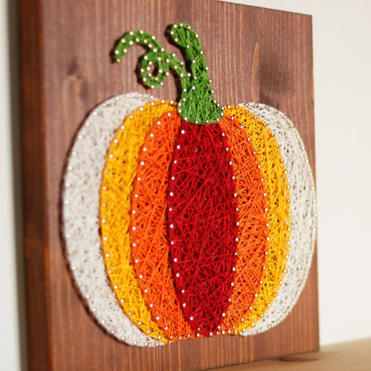 Side view of the completed pumpkin string art, featuring autumn colors and a rustic wooden background, perfect for seasonal home decor