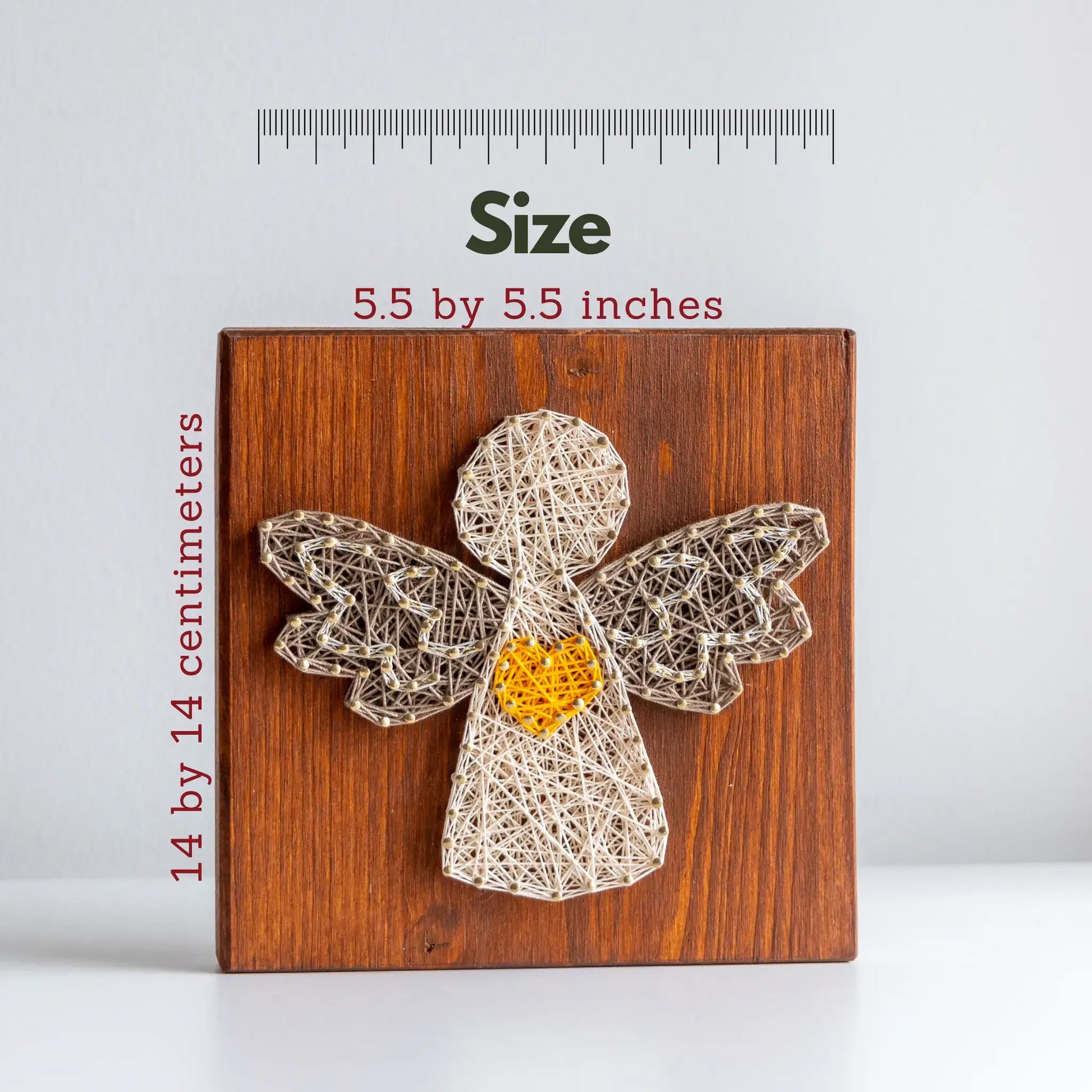 String art angel on a wooden board with measurements and a ruler