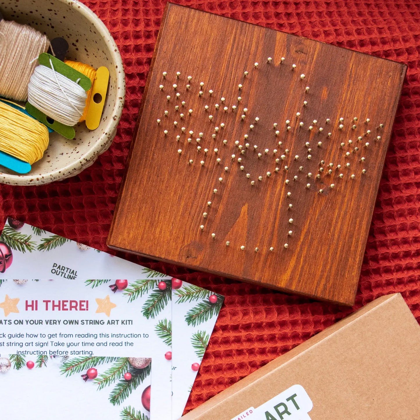 Wooden string art kit with instructions and materials on a red surface