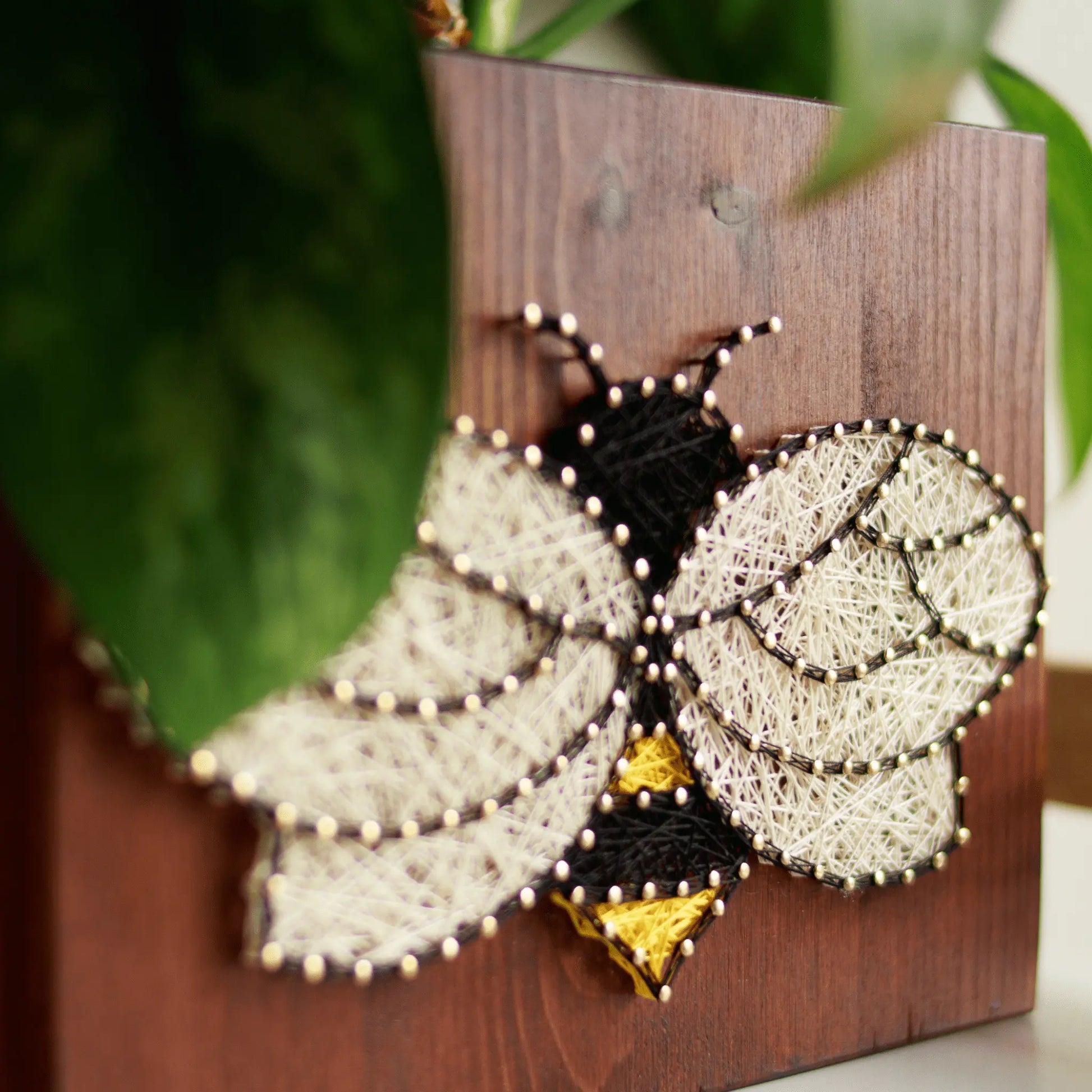 Bee string art displayed with green foliage, emphasizing the handmade details and natural theme of the design.