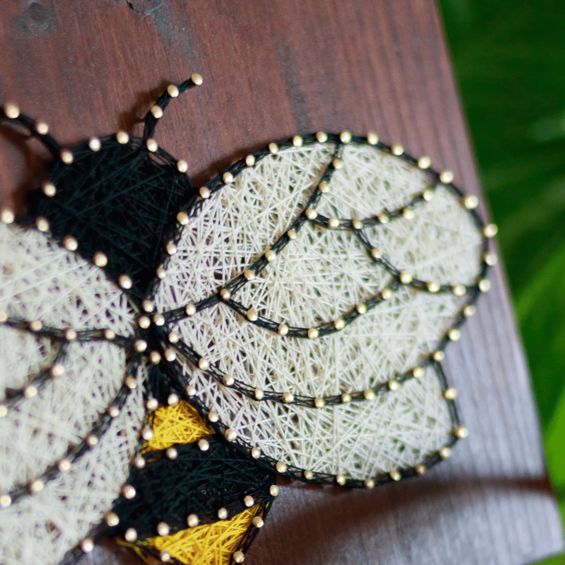 Close-up of bee string art highlighting the threading technique and detailed nail placements on a wooden background.