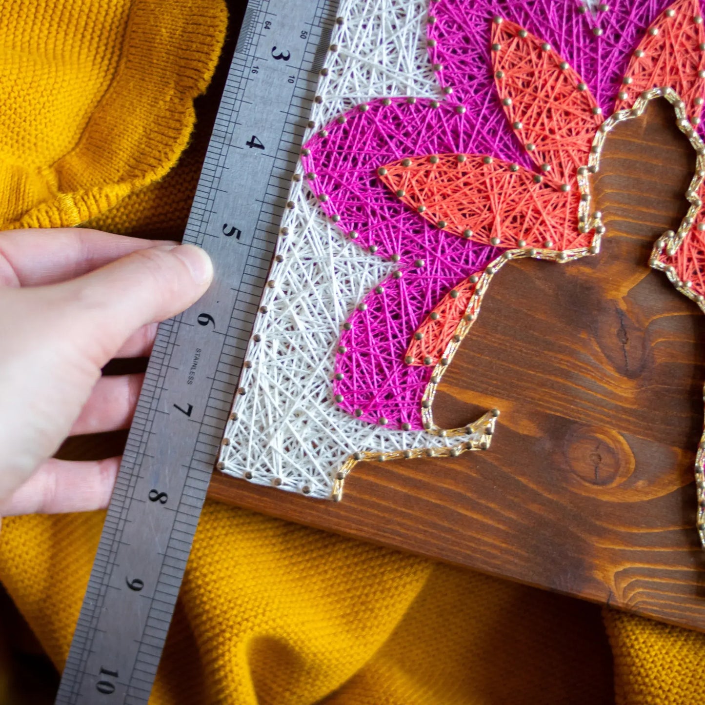 Scale view. Buddha silhouette string art with vibrant lotus petals in pink, orange, and white, mounted on a wooden background, representing a peaceful, meditation-inspired design.