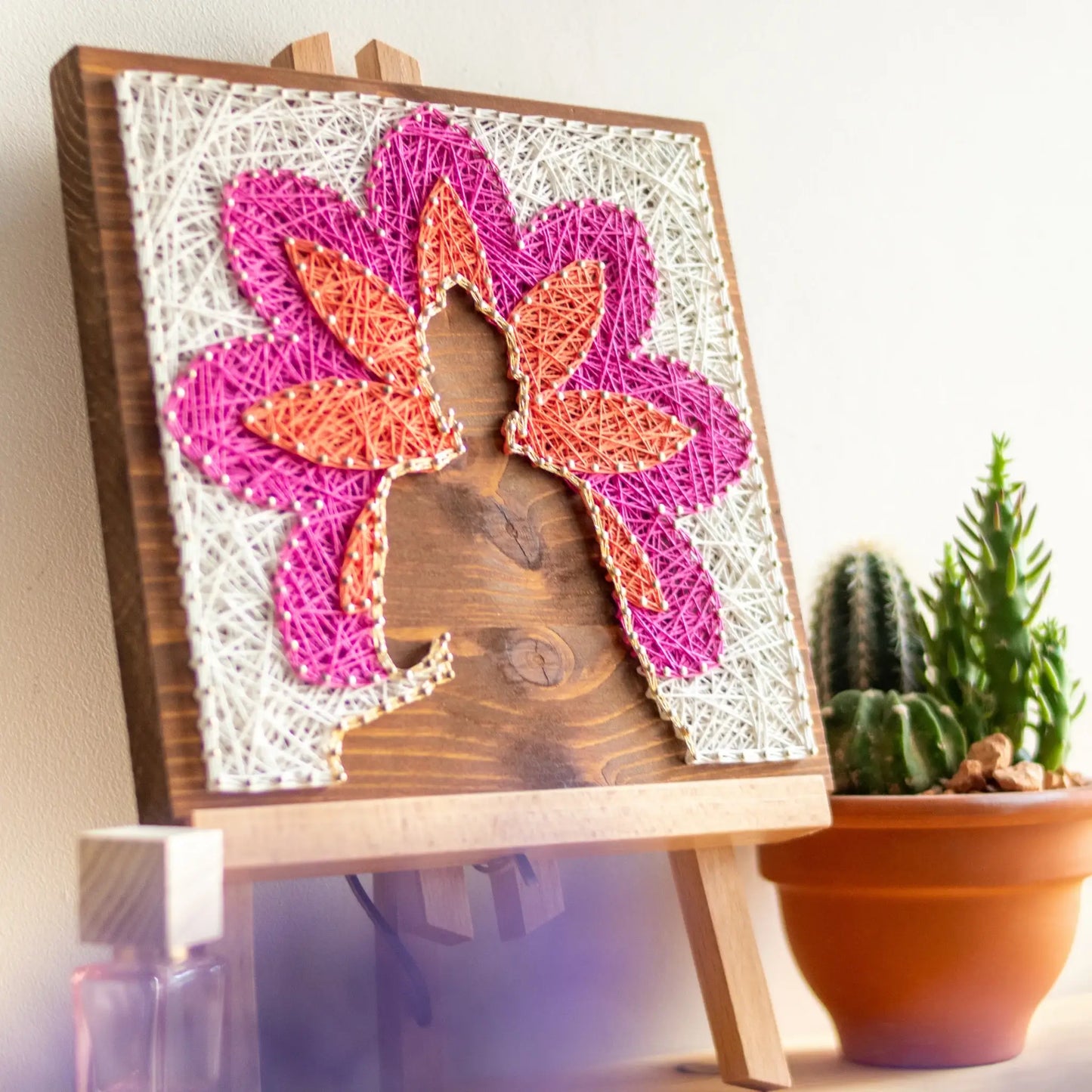 Side view. Buddha silhouette string art with vibrant lotus petals in pink, orange, and white, mounted on a wooden background, representing a peaceful, meditation-inspired design.