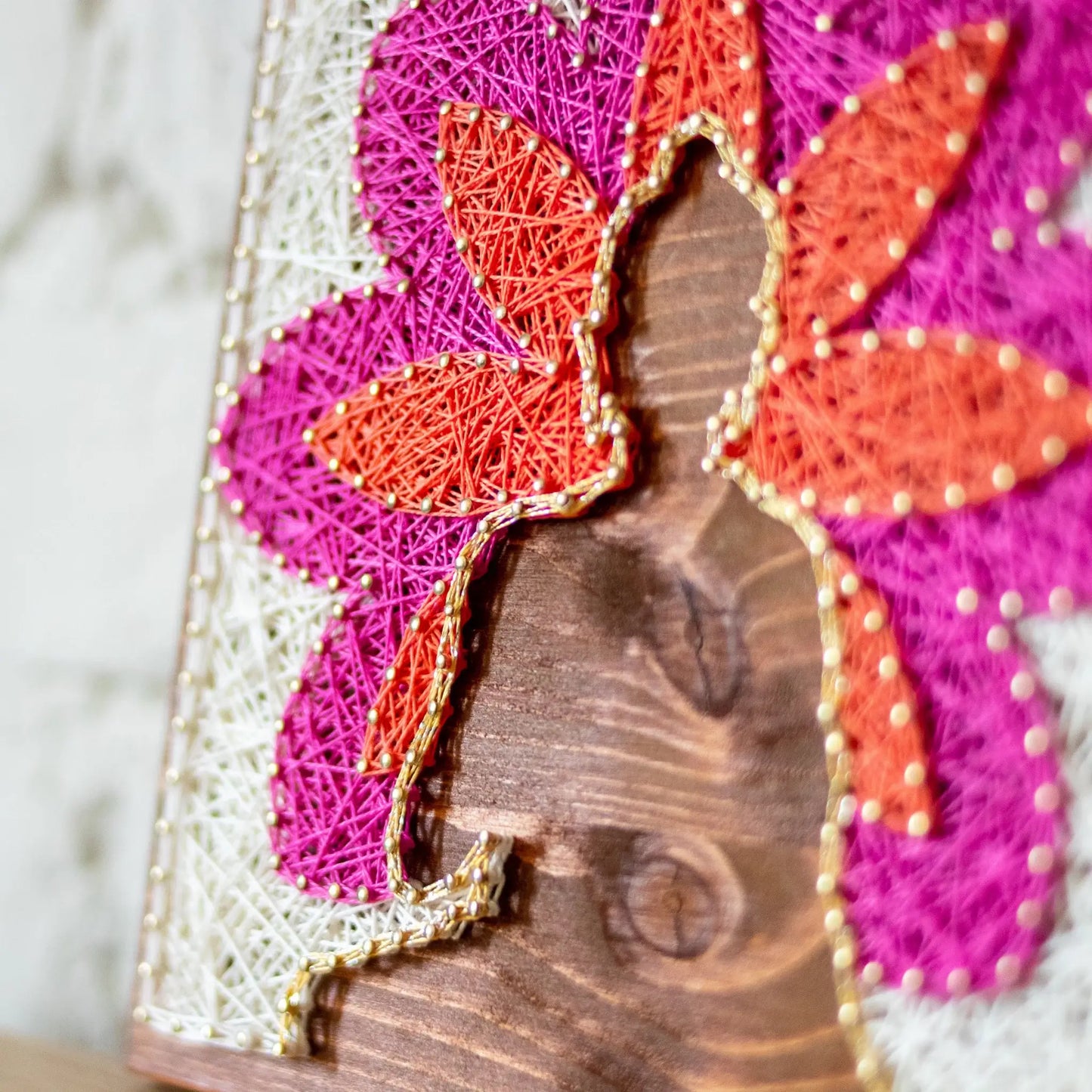 Side view. Buddha silhouette string art with vibrant lotus petals in pink, orange, and white, mounted on a wooden background, representing a peaceful, meditation-inspired design.