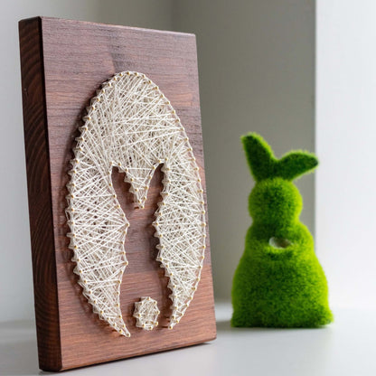Side view of bunny and egg string art pattern with a green decorative bunny figure in the background.