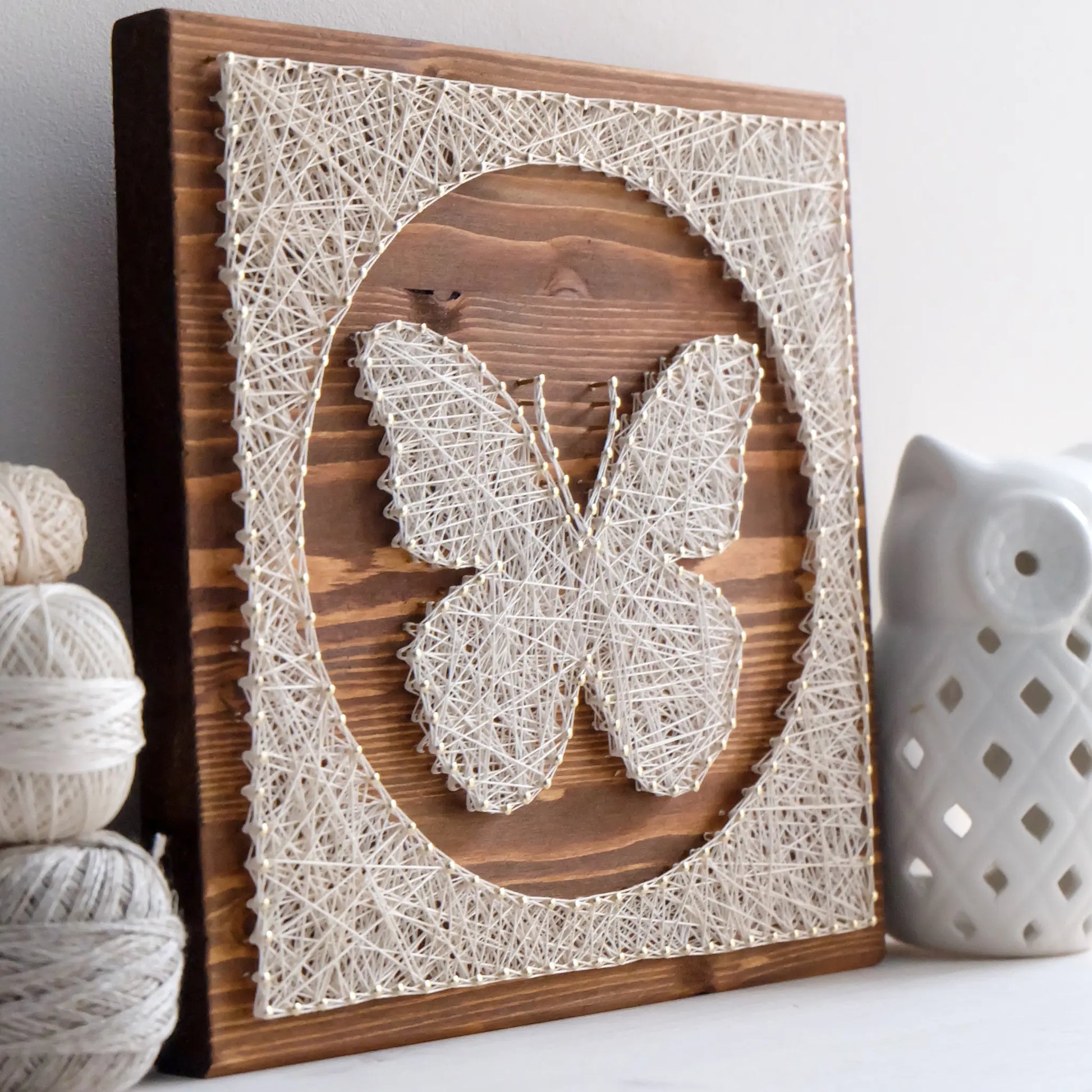 Butterfly string art displayed on a shelf with yarn and decor, part of craft kits for adults, showcasing completed DIY project.