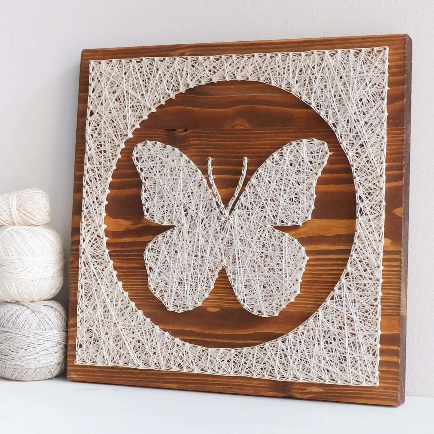 Side view of butterfly string art on display – A side view of the butterfly string art pattern design placed on a shelf, with yarn rolls beside it for decorative context.