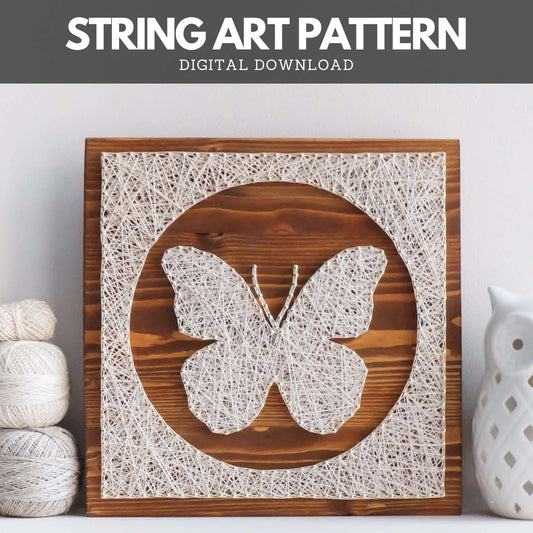 Butterfly string art pattern design displayed on a wooden board, with white thread forming a detailed butterfly silhouette. The design is framed in a circular string border, next to yarn and ceramic decor.