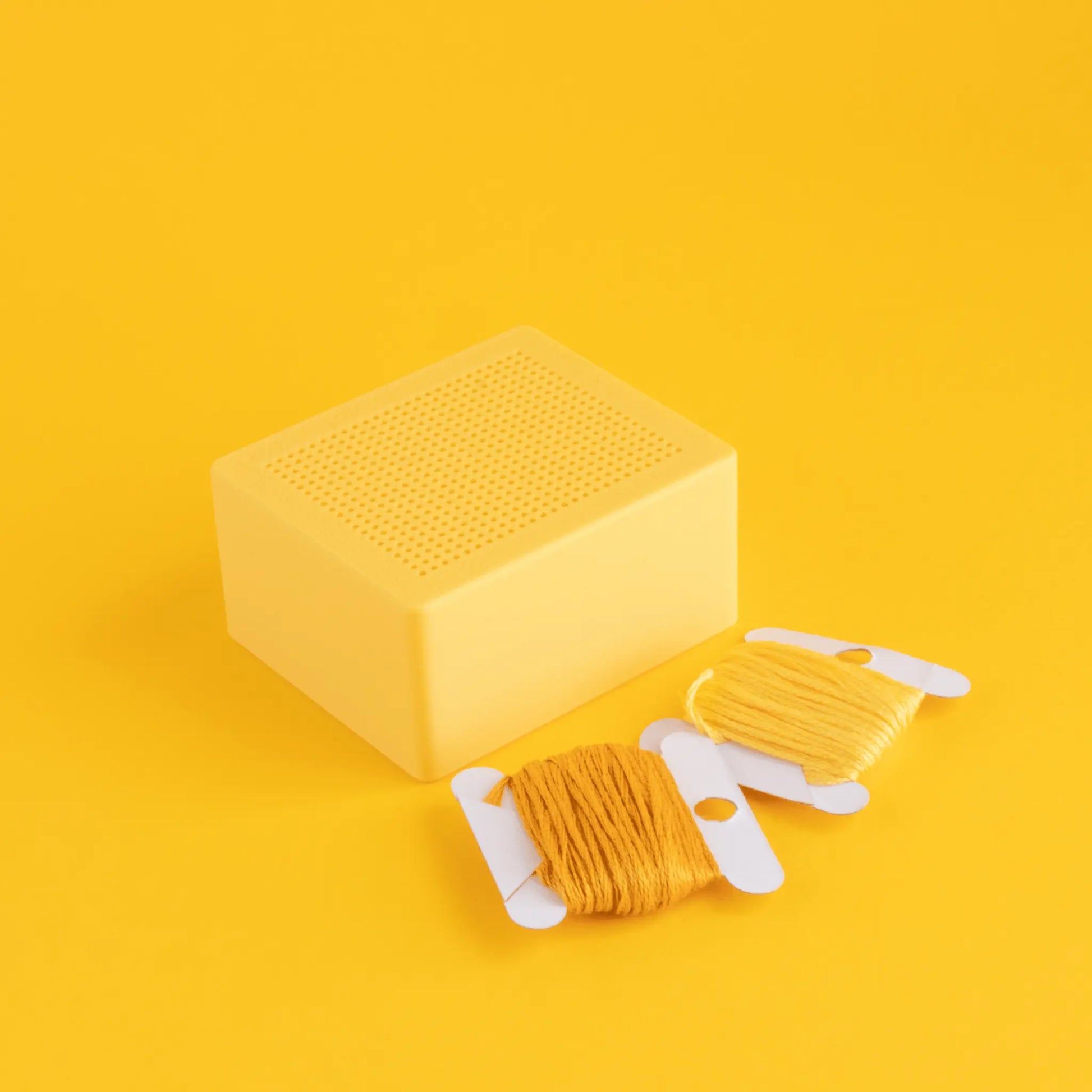 Cross stitch box blank with stitchable lid and embroidery floss on a yellow background, embroidery base for small cross stitch and hand embroidery projects.