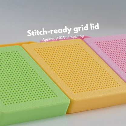 Close-up of stitch-ready grid lids on cross stitch boxes in green, yellow, and pink, showing evenly spaced holes comparable to AIDA 11 spacing
