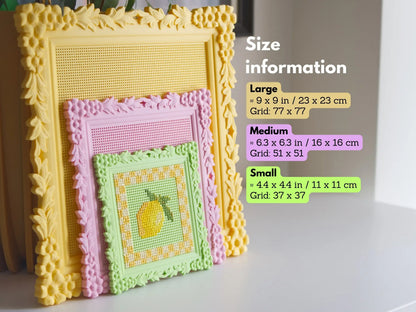 Three ornate square 3D-printed cross stitch frames stacked to compare the large yellow, medium pink, and small green sizes. The small frame features a stitched lemon, while the larger grids are blank.