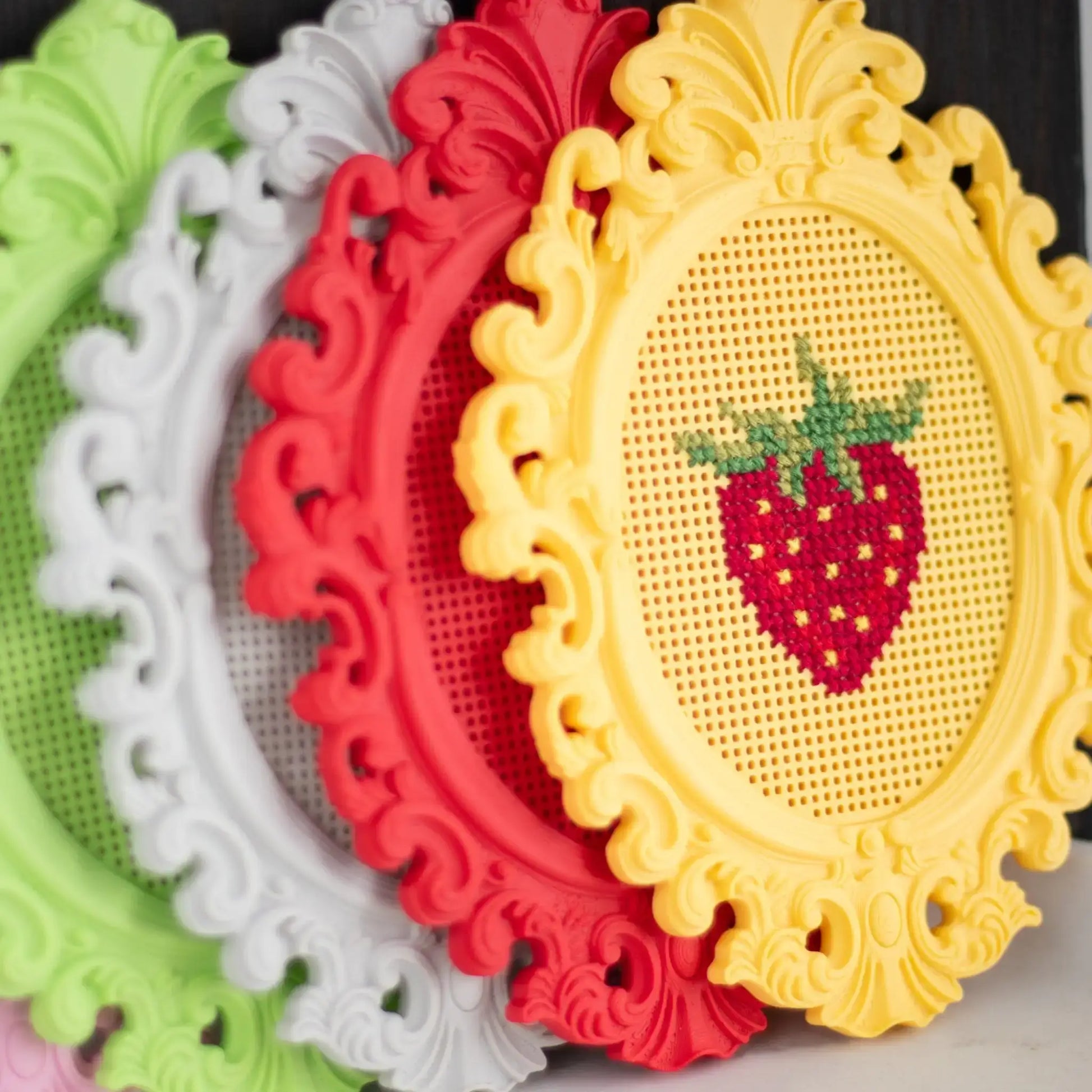 Overlapping stitchable cross stitch frames in multiple colors, highlighting the decorative frame shape and a finished strawberry cross stitch design.