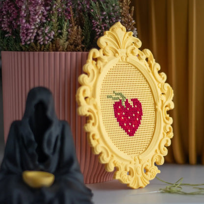 Stitchable cross stitch frame with a finished strawberry design, shown styled on a shelf as a decorative display piece.