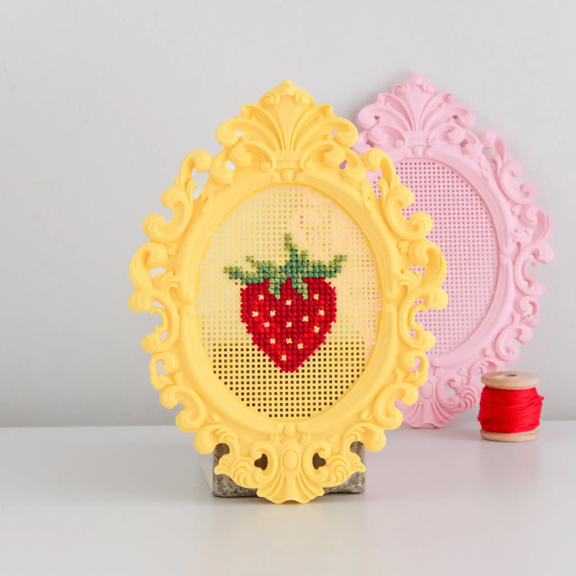 Stitchable cross stitch frame with an ornate yellow border, showing a finished strawberry cross stitch design displayed upright.