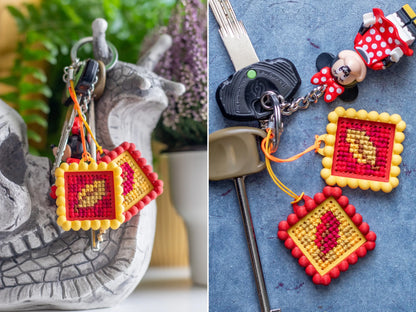 Two red and yellow keychain charms with contrasting stitched motifs, styled on a set of car keys, shown hanging from a snail figurine and lying on blue stone.