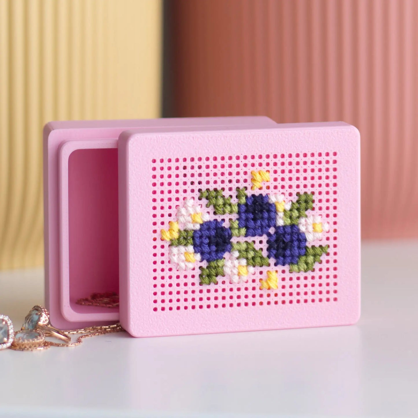 Pink stitchable cross stitch box with floral design on the lid, shown open with jewelry inside