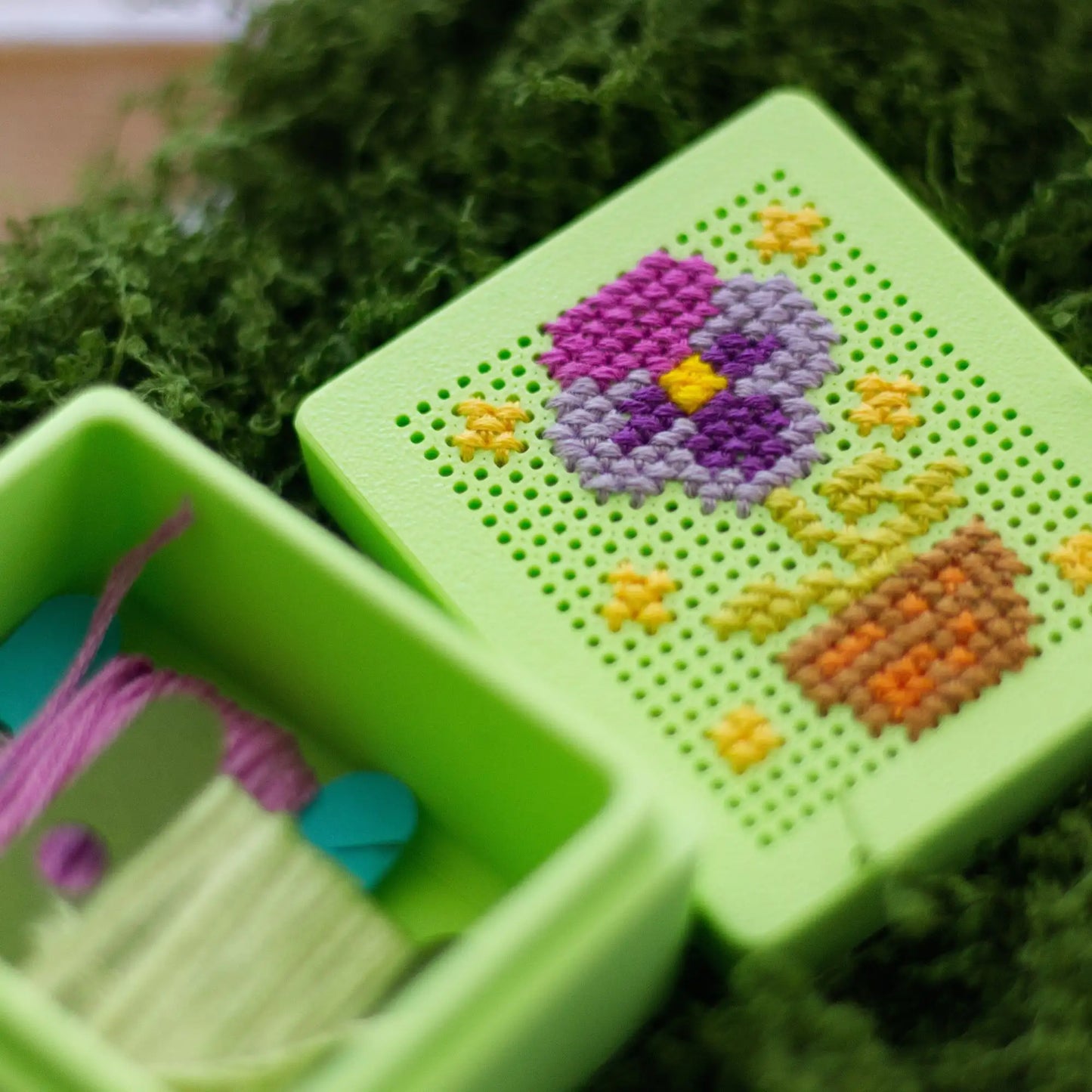Green stitchable cross stitch box with floral design on the lid, shown open with thread stored inside