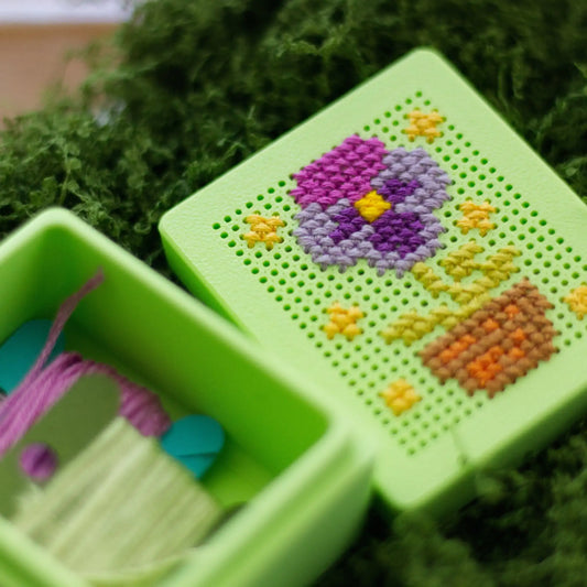 Green stitchable cross stitch box with floral design on the lid, shown open with thread stored inside