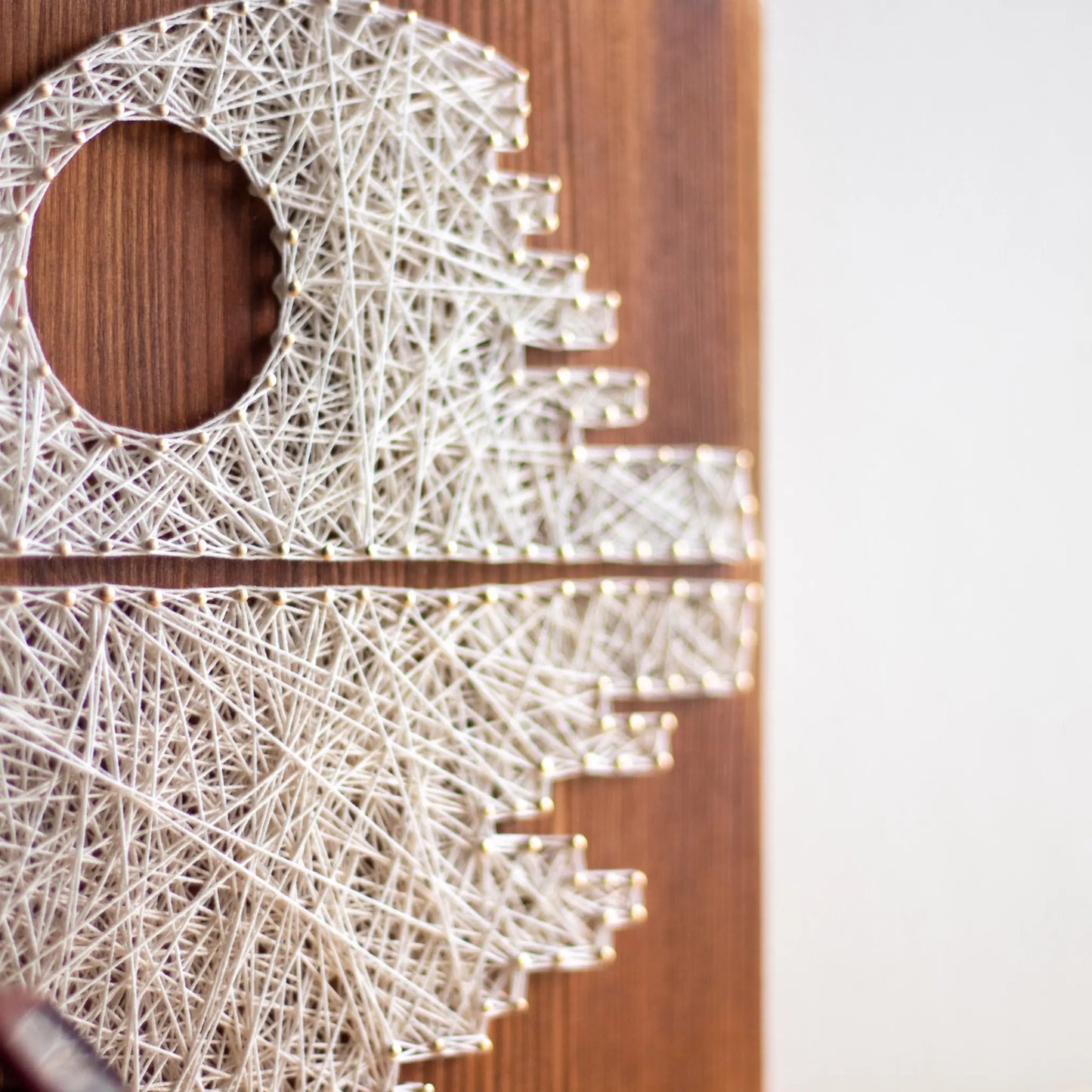 DIY string art kit featuring a Death Star design with white threads on a brown wooden board by GoodStrings - view from side