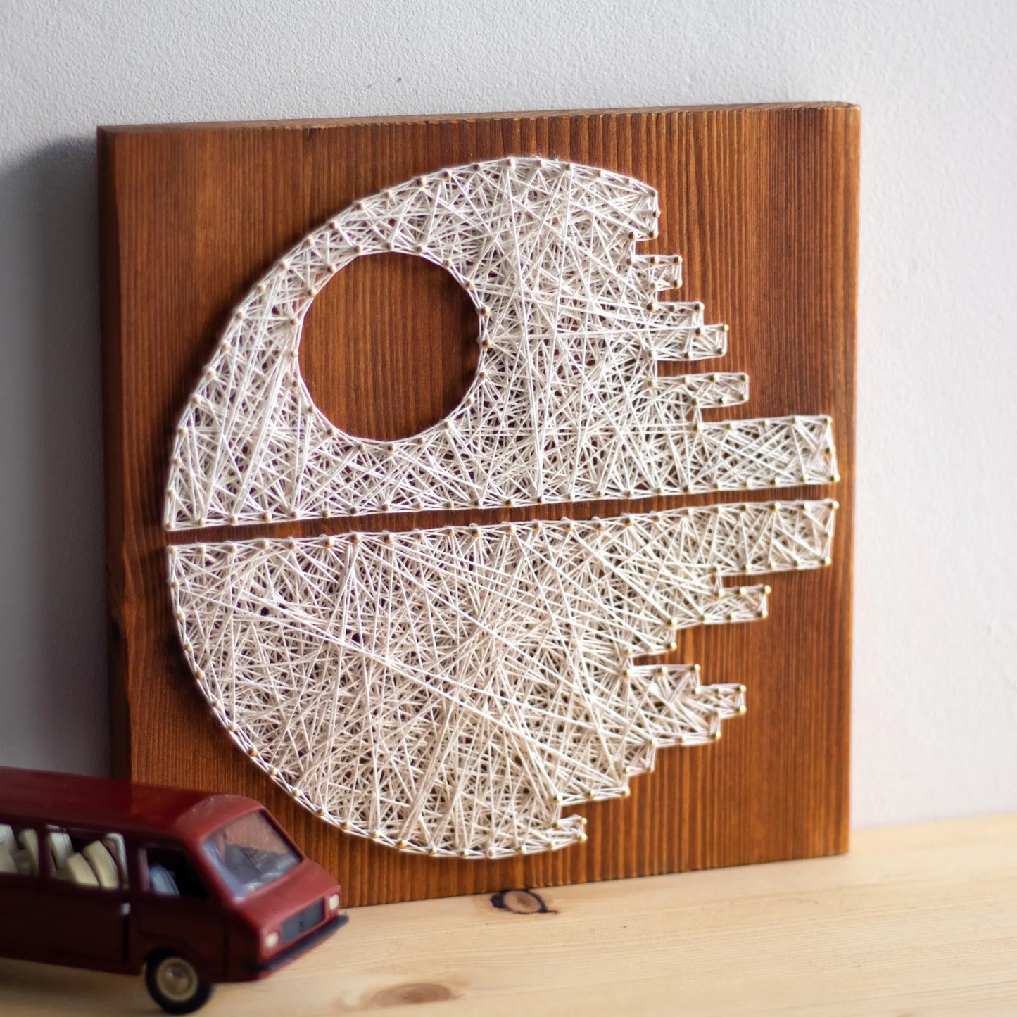 DIY string art kit featuring a Death Star design with white threads on a brown wooden board by GoodStrings