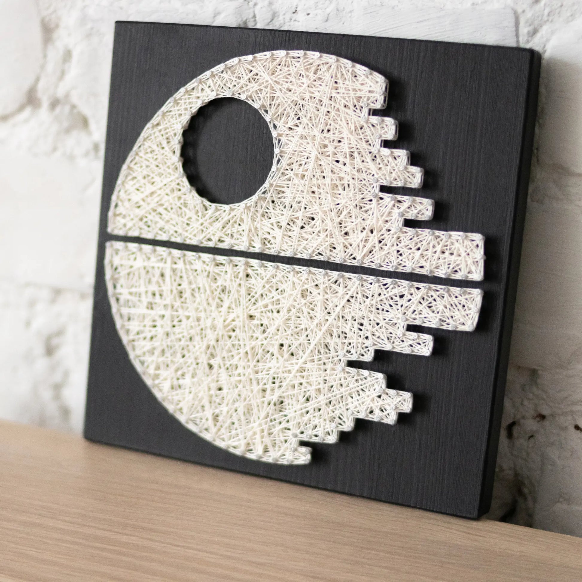 DIY string art kit featuring a Death Star design with white threads on a black wooden board by GoodStrings side view