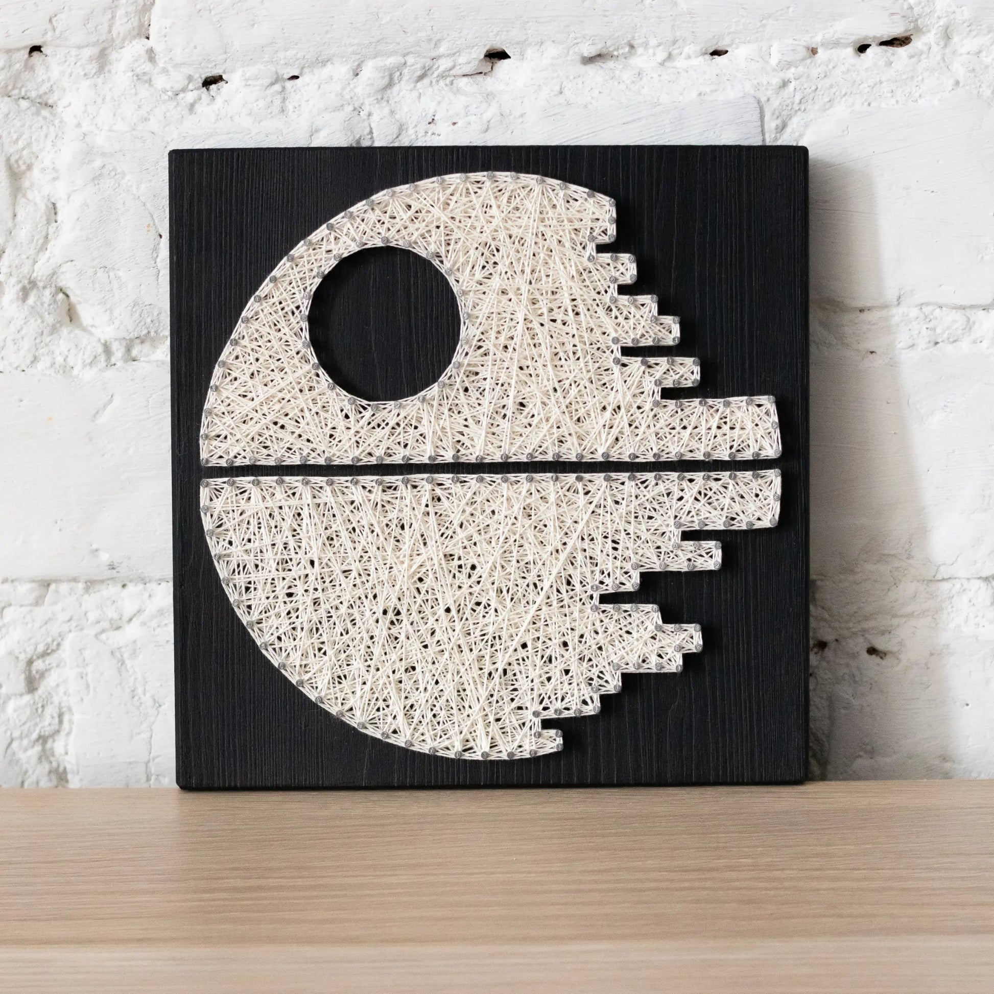 DIY string art kit featuring a Death Star design with white threads on a black wooden board by GoodStrings front view