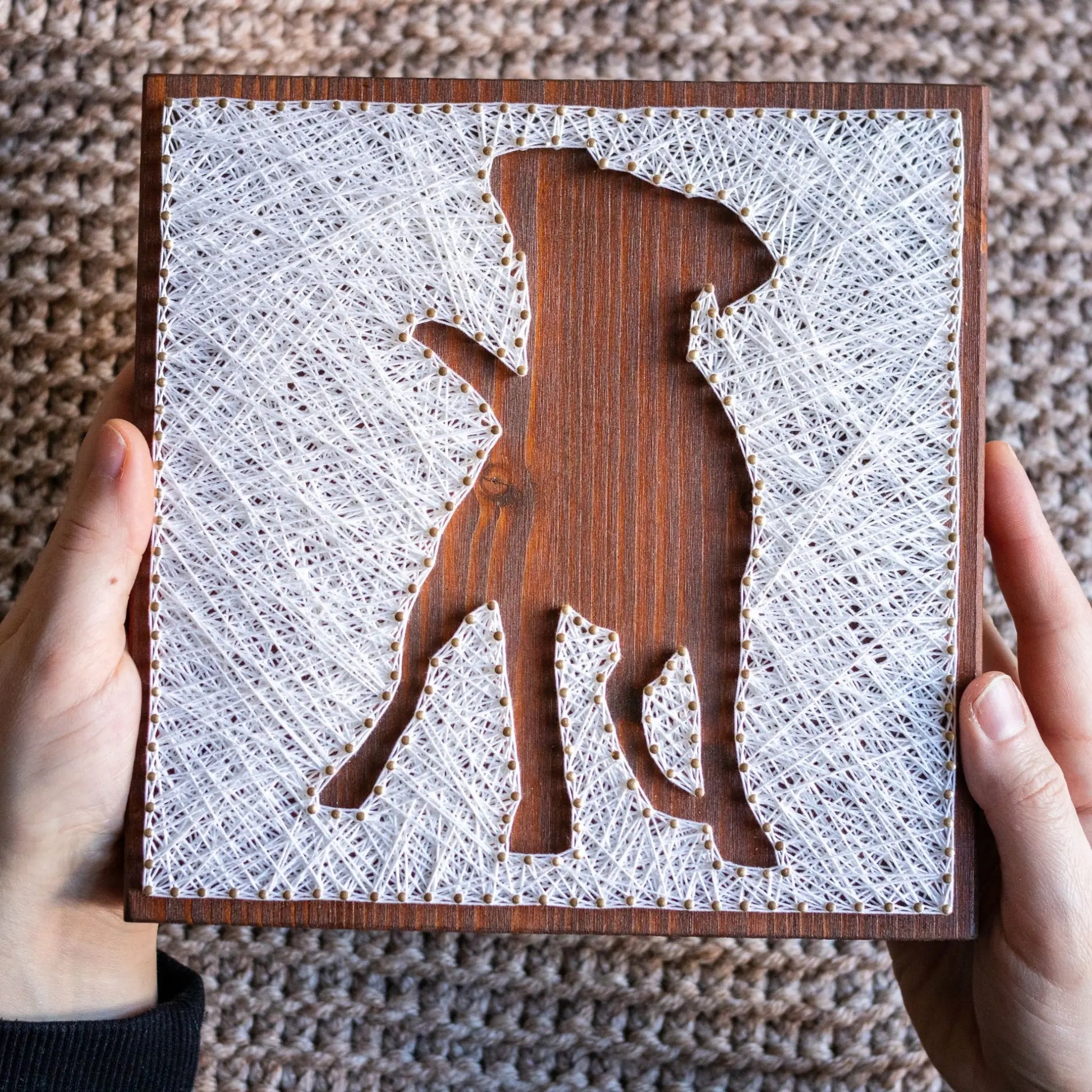 DIY string art kit featuring a dog silhouette outlined with white thread on a rustic wooden board by GoodStrings - held in hands, top view