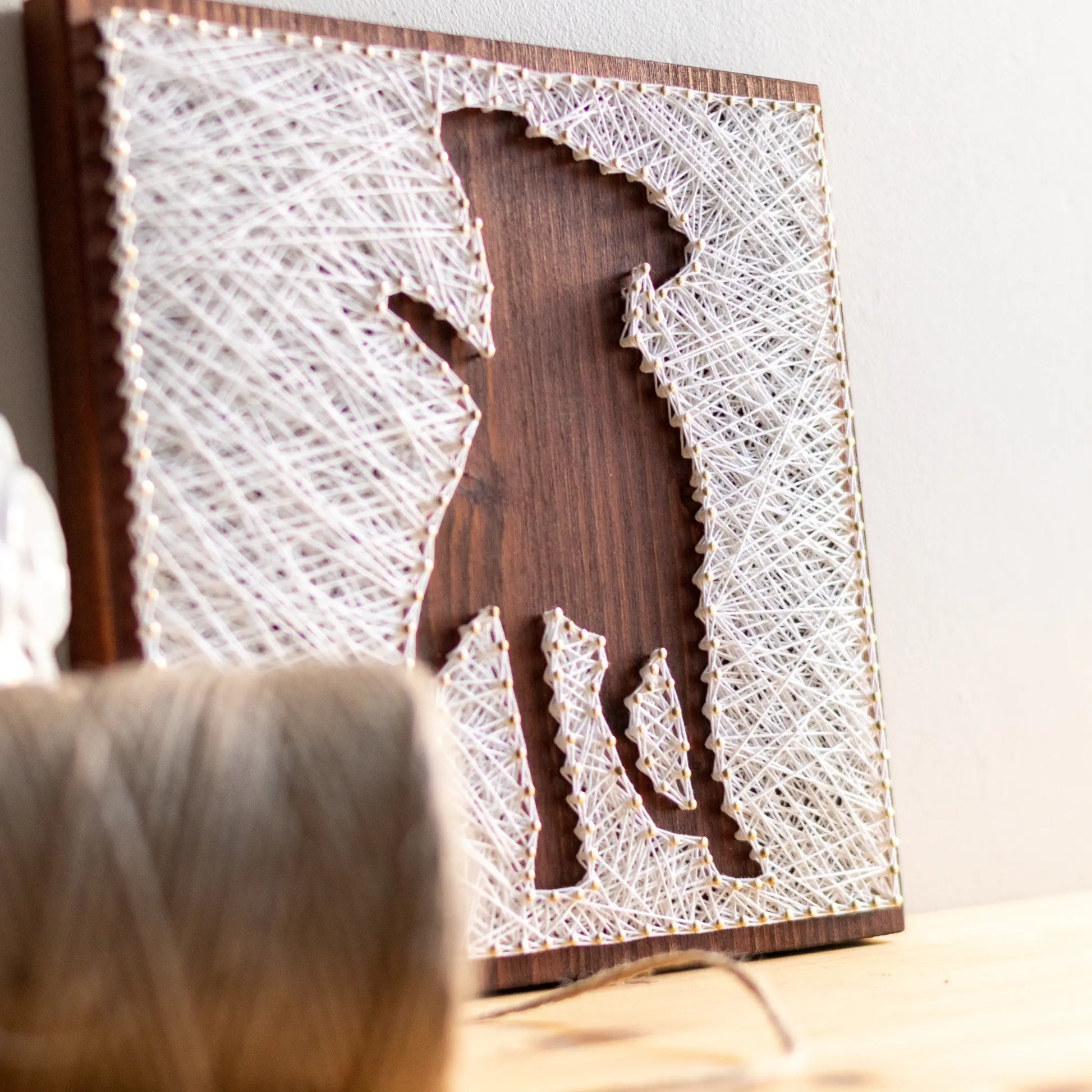 DIY string art kit featuring a dog silhouette outlined with white thread on a rustic wooden board by GoodStrings side view