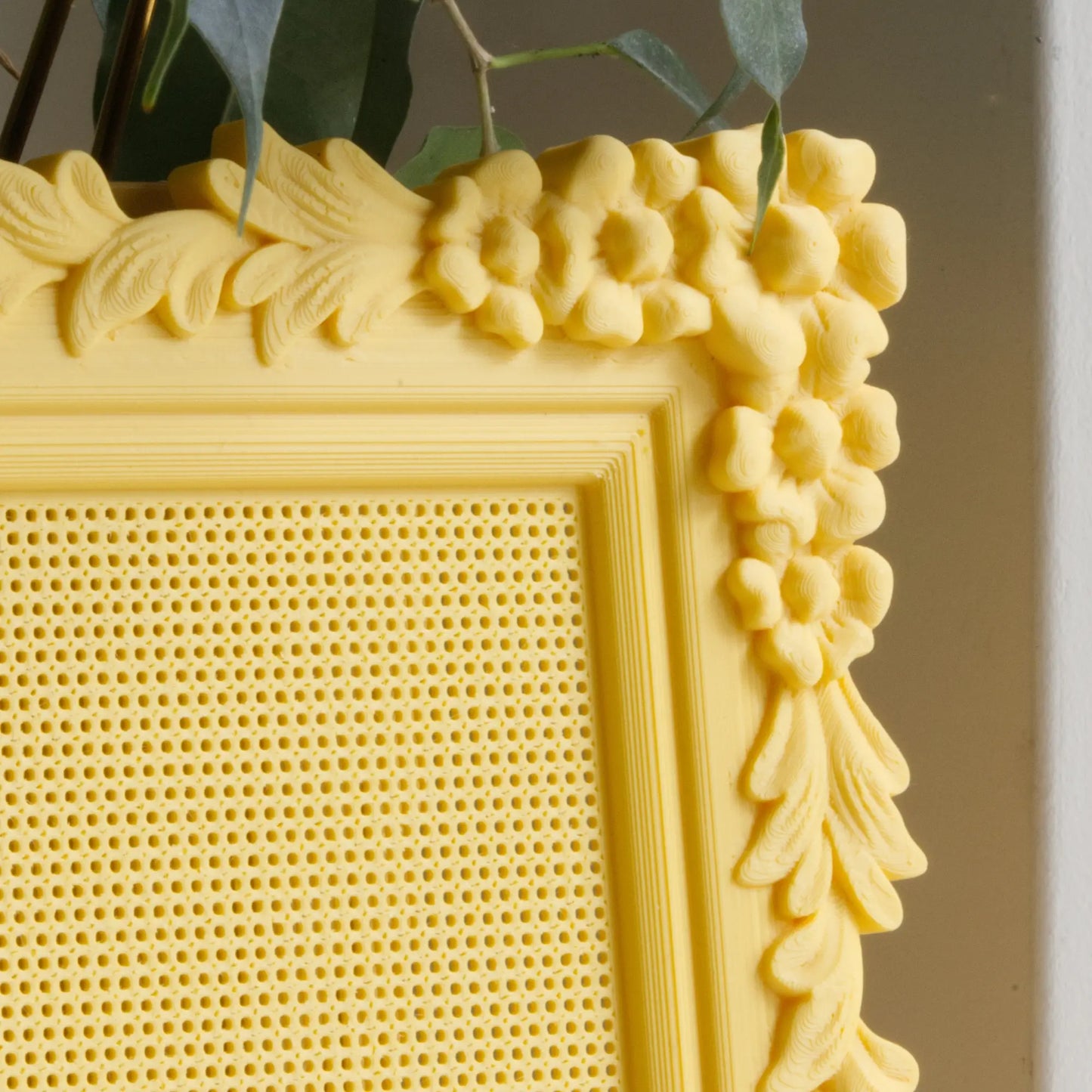 Close-up of the yellow floral cross stitch frame corner, showing the ornate flower trim and the perforated stitchable grid.
