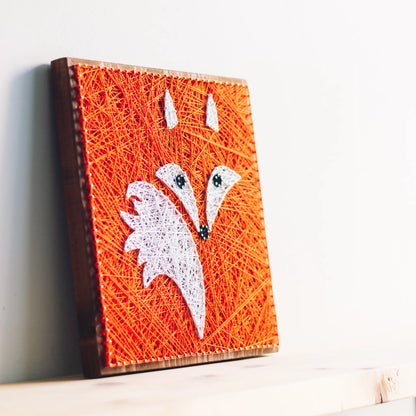 Handcrafted fox string art on a wooden board, featuring vibrant orange and white threads forming a fox face.