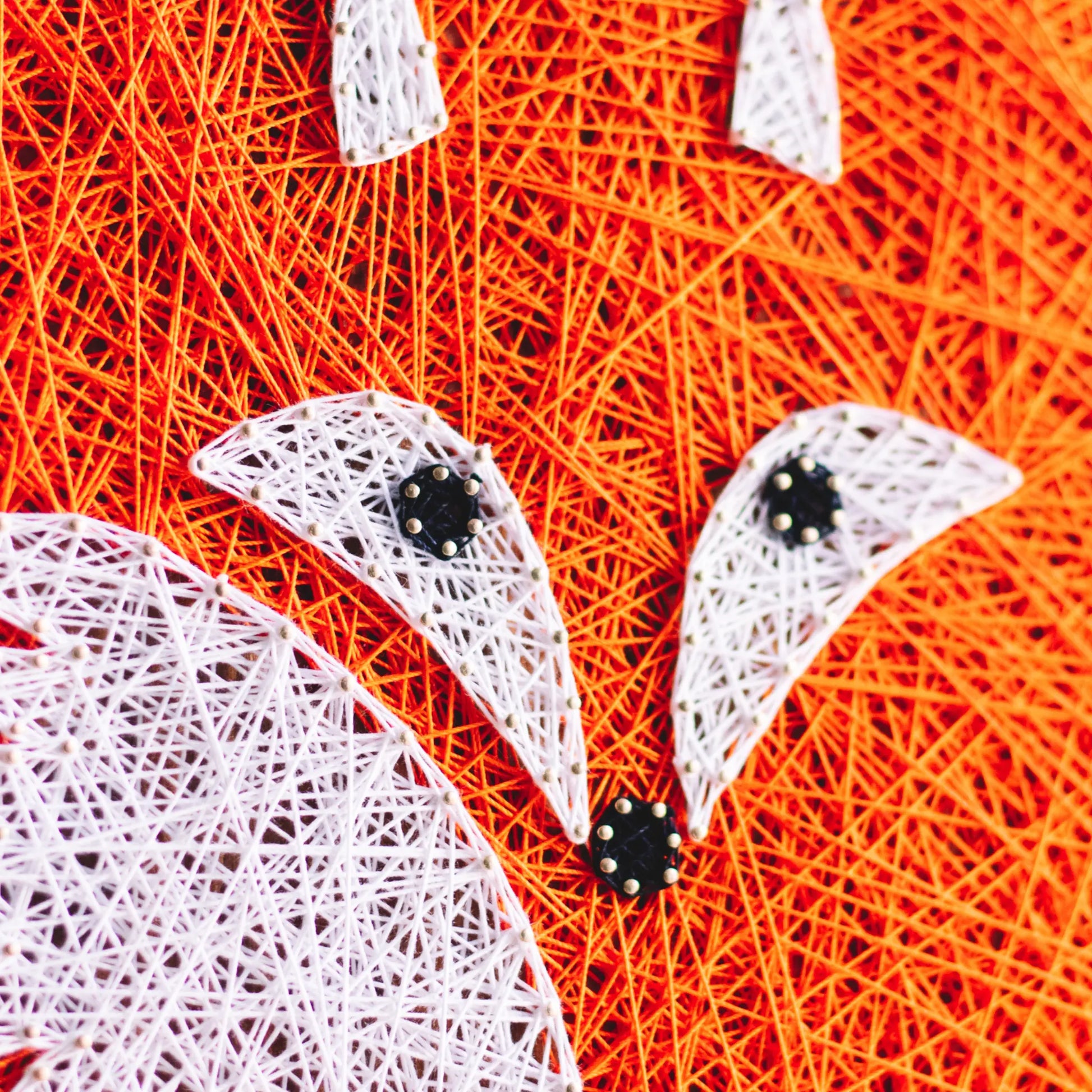 Handcrafted fox string art on a wooden board, featuring vibrant orange and white threads forming a fox face.