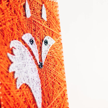 Handcrafted fox string art on a wooden board, featuring vibrant orange and white threads forming a fox face.