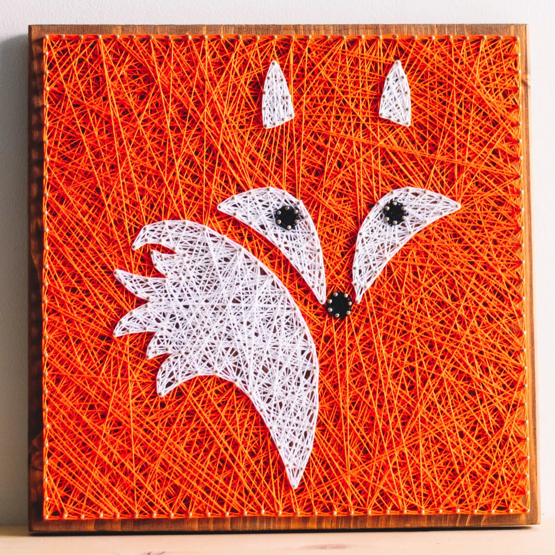 Handcrafted fox string art on a wooden board, featuring vibrant orange and white threads forming a fox face.