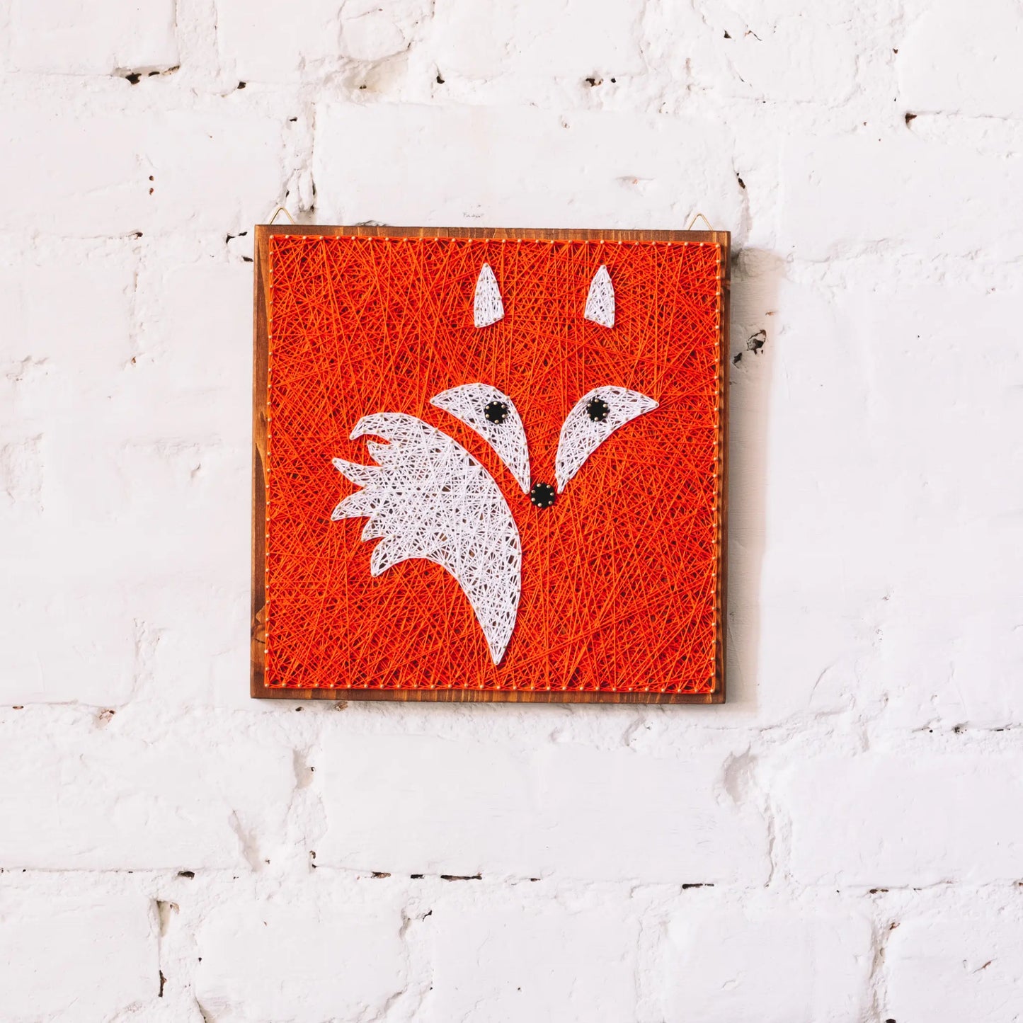 Handcrafted fox string art on a wooden board, featuring vibrant orange and white threads forming a fox face.